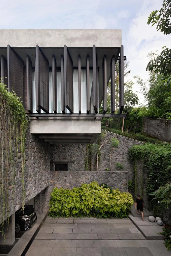 An exterior view of a modern architectural house with concrete walls and a greenery garden.
