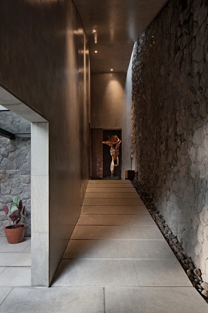 A modern, minimalist corridor made of concrete and adorned with stone walls and plants.