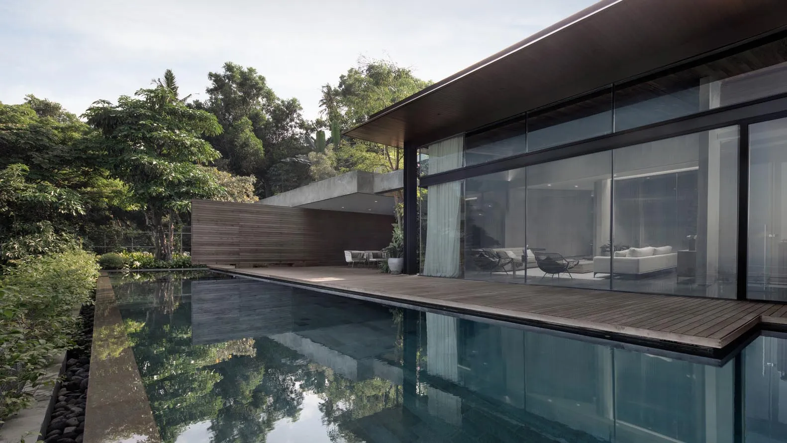 Modern residential exterior featuring glass and wood materials, with a pool in front of the house.