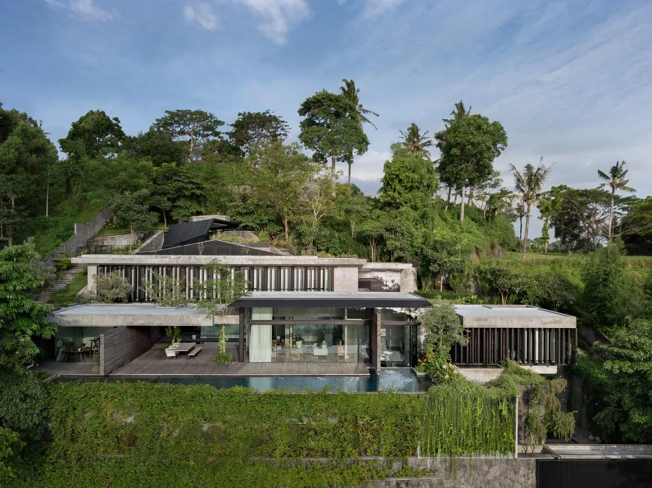 Modern residential house with a concrete and glass exterior on a green hillside.