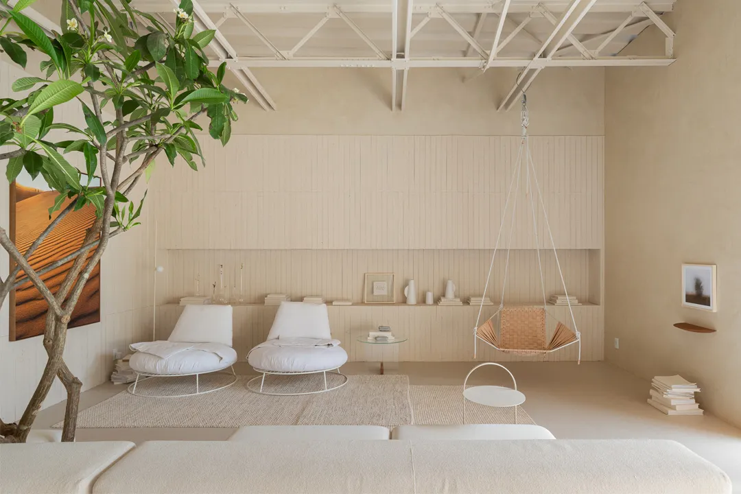 A minimalist living room with concrete floors, white seating, and a hanging swing chair.