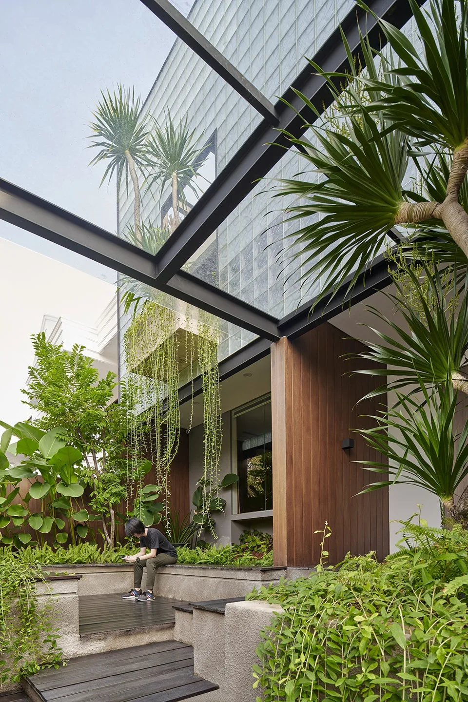 A modern housefront featuring large glass panels, wooden accents, and lush greenery.