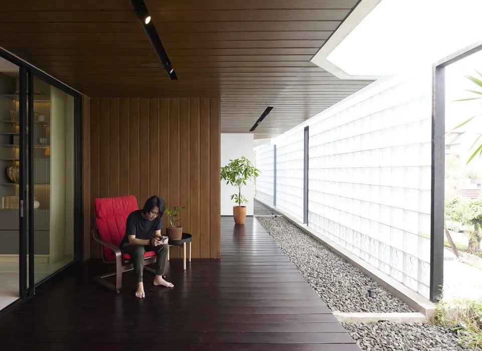 A person sits on a red cushioned chair in a modern porch space with a striped wooden floor, green plant in a terracotta pot,