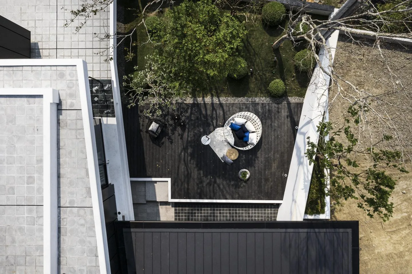 Modern residential patio with wooden deck and outdoor furniture, surrounded by greenery and trees.