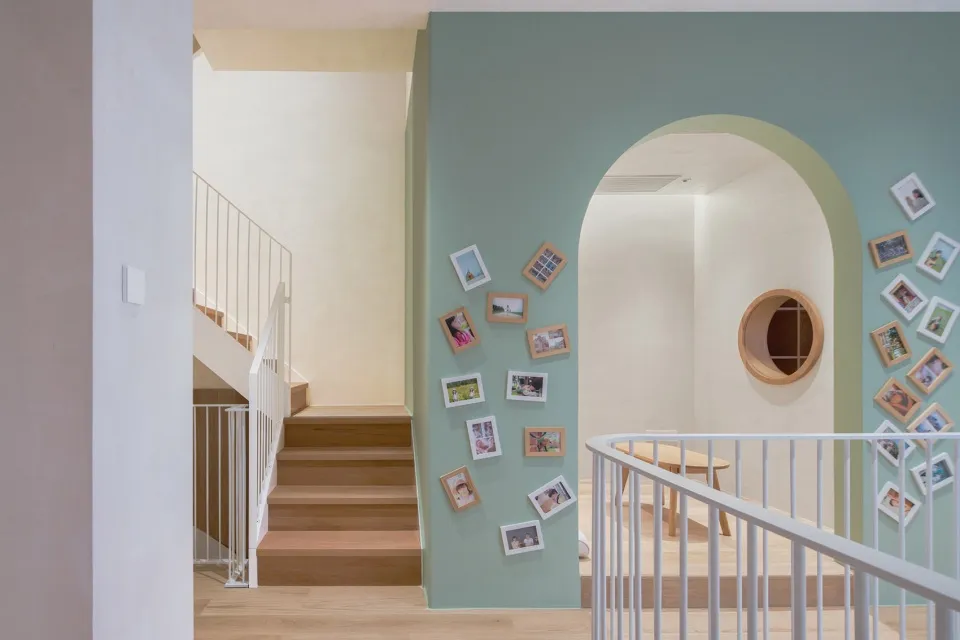 A wooden staircase with a railing, framed photos on the wall, and a table with chairs.