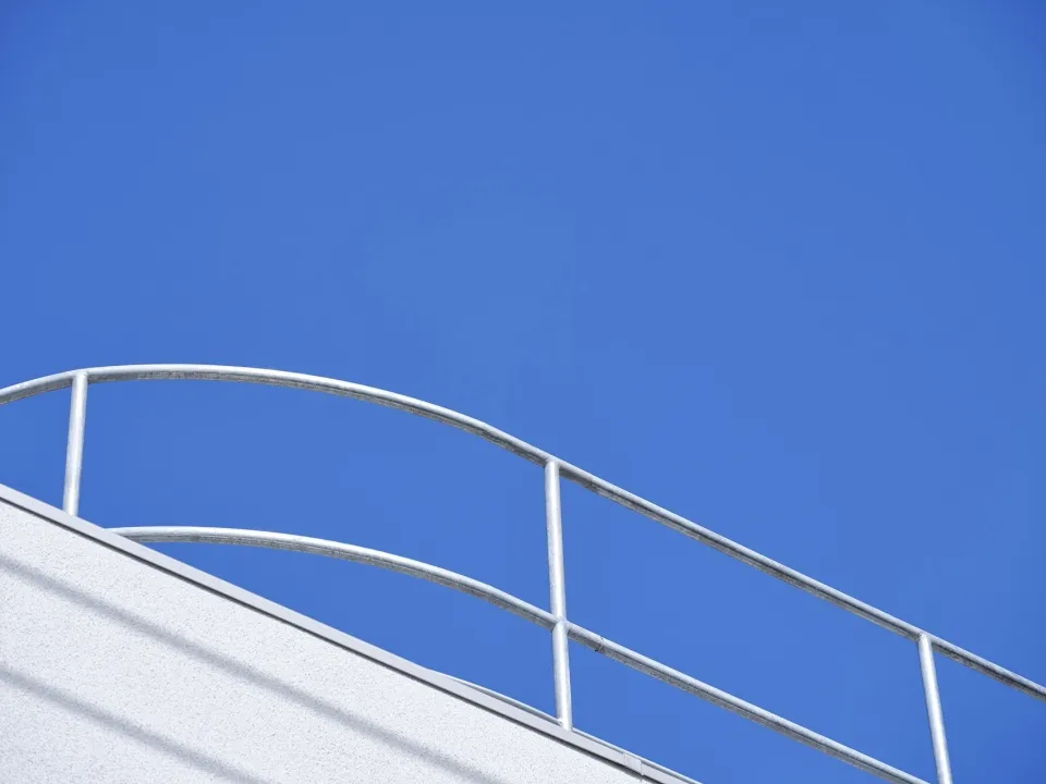 A minimalist architectural detail featuring a metal railing against a clear blue sky.