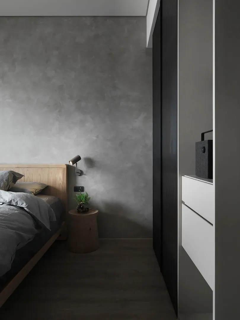 A minimalist bedroom with concrete walls and wooden furniture.
