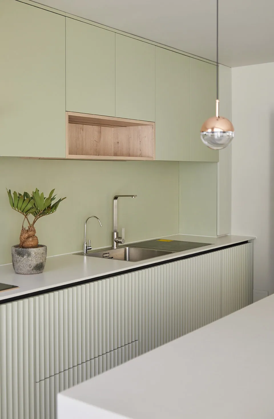 A modern kitchen with green cabinets, a sink, and a plant.