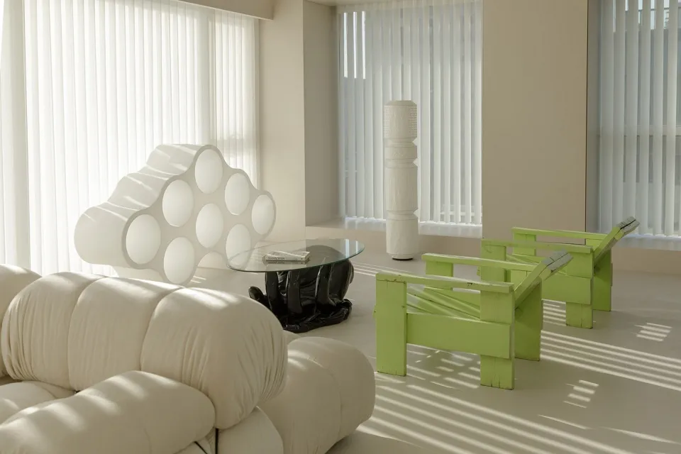 A minimalist living room with white furniture, green chairs, and a glass coffee table.