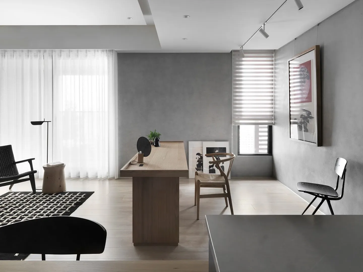 A modern home office with concrete walls, a wooden desk, and a glass window.