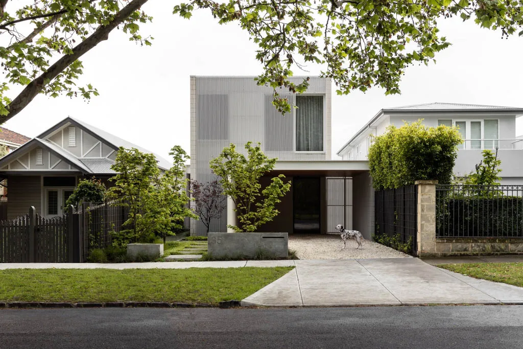 A modern residential exterior featuring a metal and concrete facade with large window blinds.