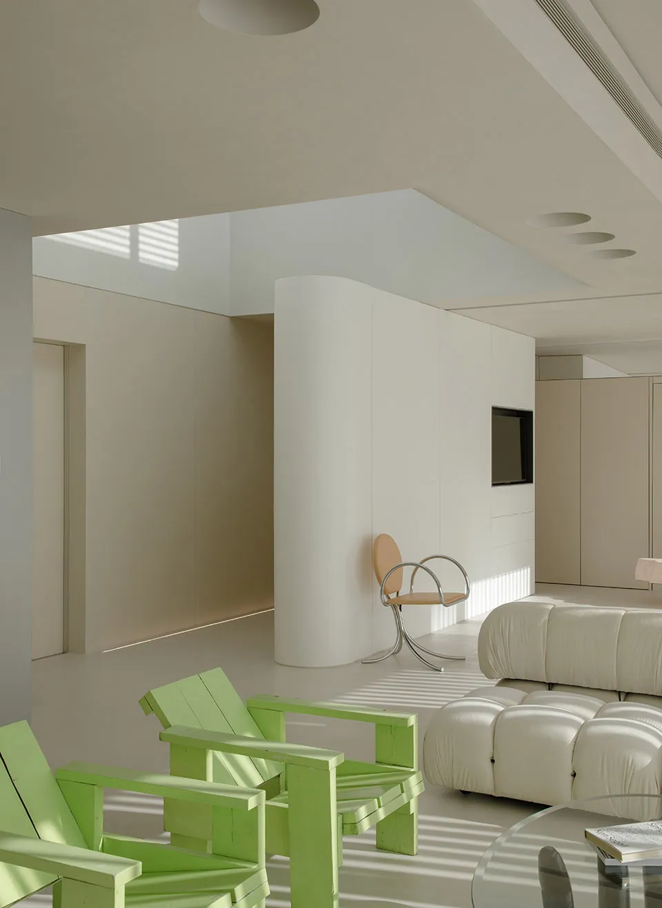 A modern living room featuring a modular sofa with green accents and neutral-colored surroundings.