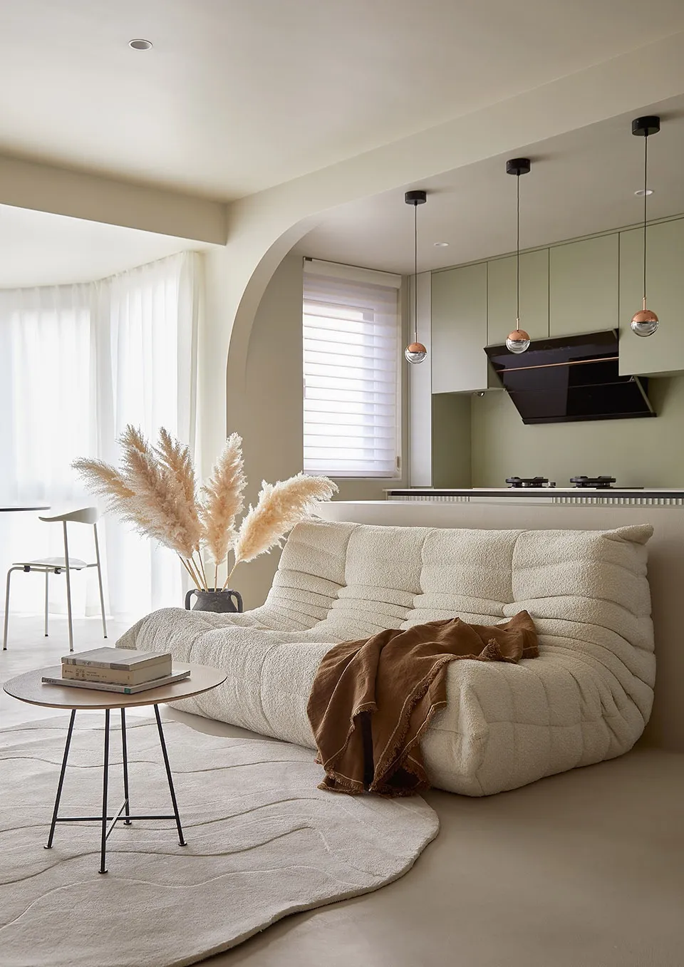 A minimalist living room featuring a textured cloth sofa, pampas grass, and a small wooden table.