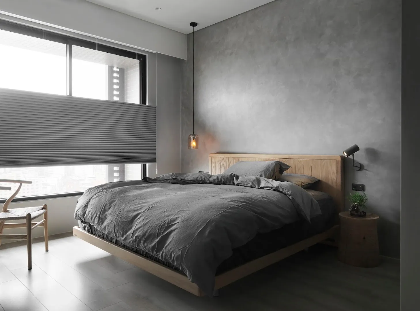 A minimalist bedroom with concrete walls, a wooden bed frame, and gray bedding.