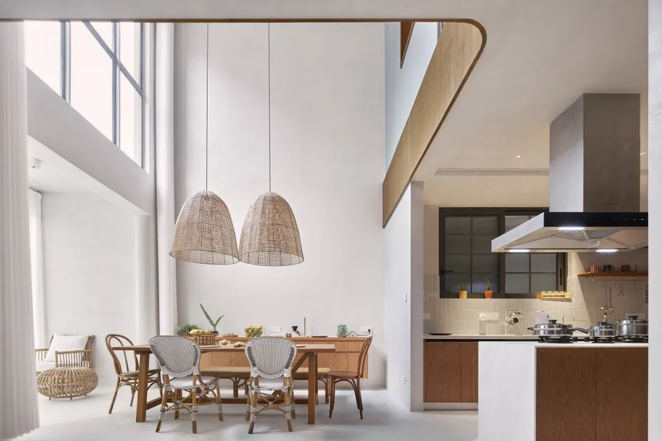 A modern, minimalist residential kitchen with concrete walls, wood cabinets, and rattan pendant lights.