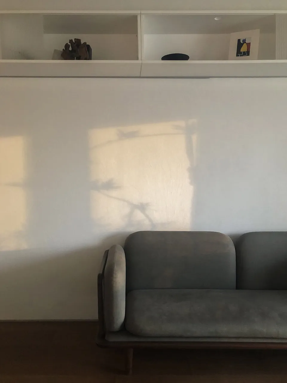 A modern neutral living room with a gray sofa and a wall-mounted shelf.