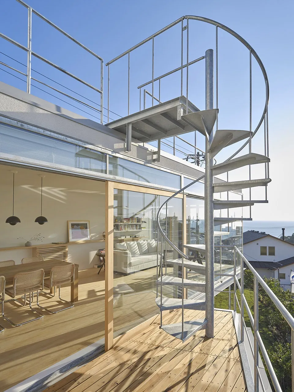 Modern residential home featuring glass, steel, and wood materials, with spiral staircase and outdoor balcony overlooking a c