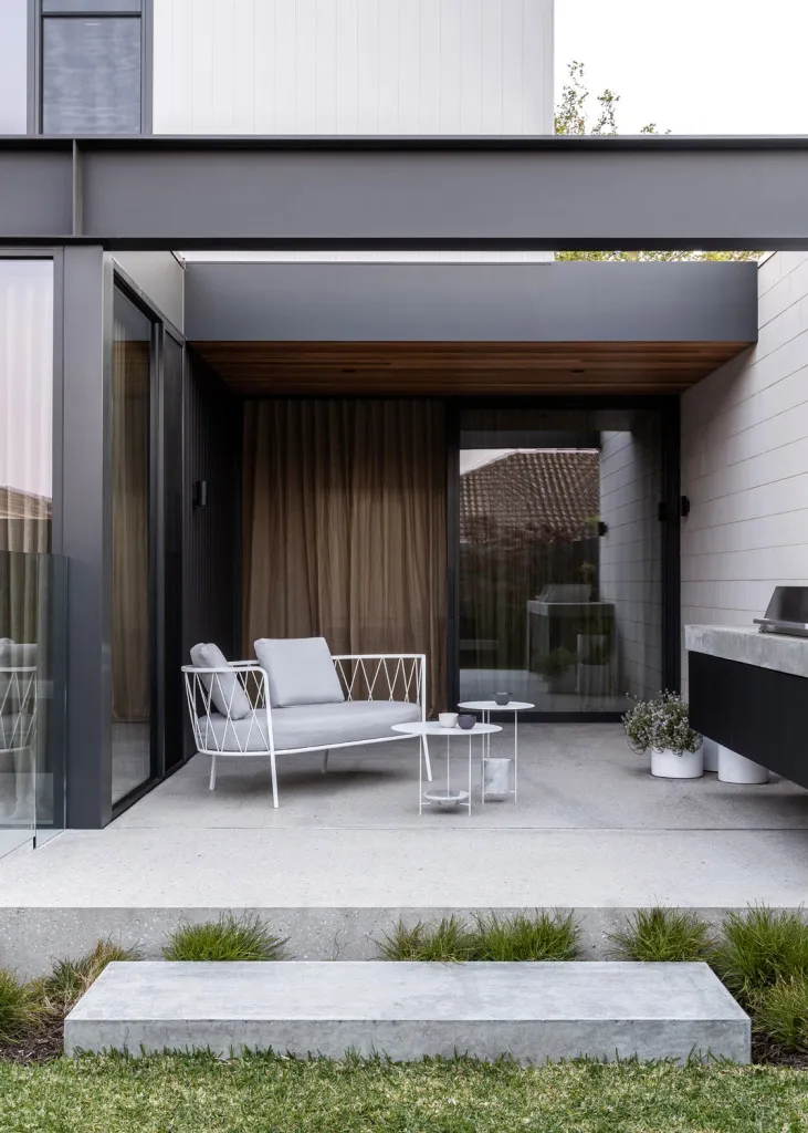 Modern industrial outdoor lounge area featuring a white metal chair with light grey cushions, a metal coffee table, and potte