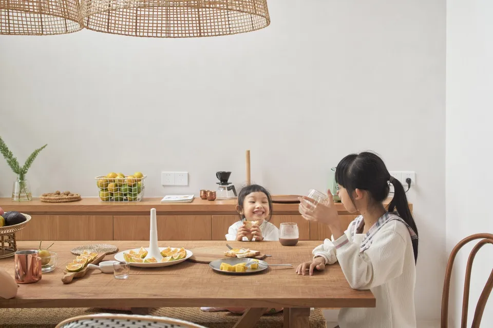 Wooden dining table with fruit and drinks in a minimalist dining room setting.