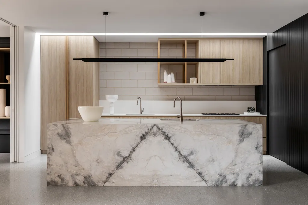 Modern industrial kitchen featuring a marble island counter with sink and faucet, wood cabinetry, and a black pendant light f