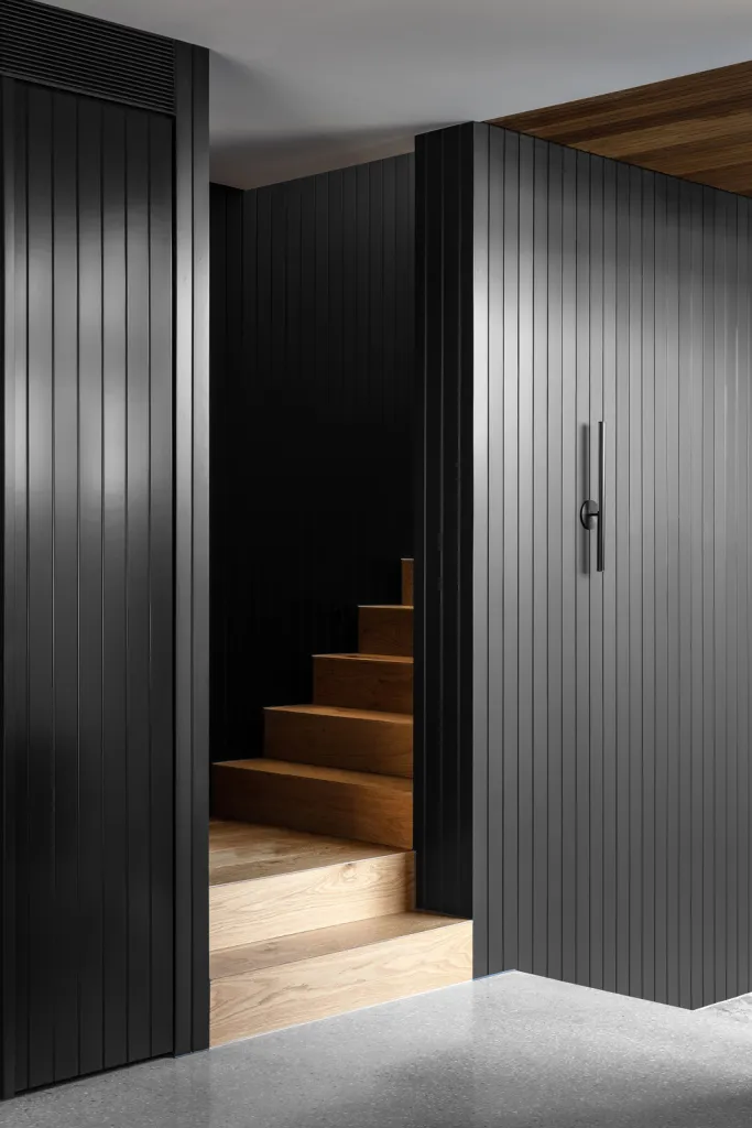 Minimalist interior design featuring black metallic panels and wooden stairs.