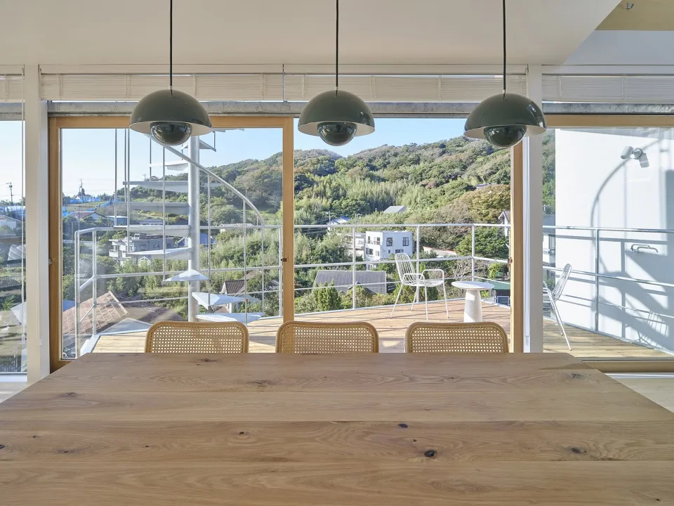 A modern minimalist dining room featuring wooden furniture and a large window overlooking a scenic landscape.
