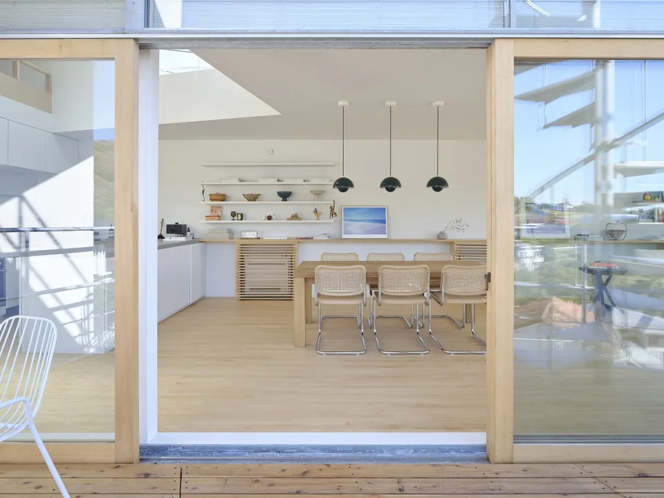 A modern, minimalist residential kitchen featuring wood, glass, and metal materials.
