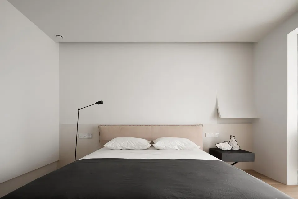A minimalist bedroom with a large bed, two pillows, a lamp, and a nightstand.