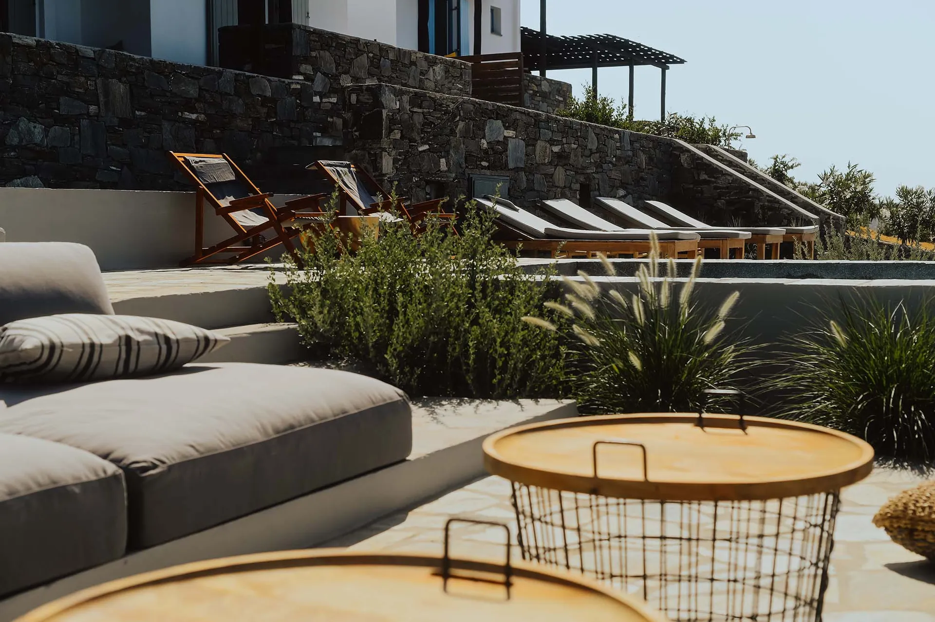 Concrete patio with wooden lounge chairs, cushions, and metal wire basket.