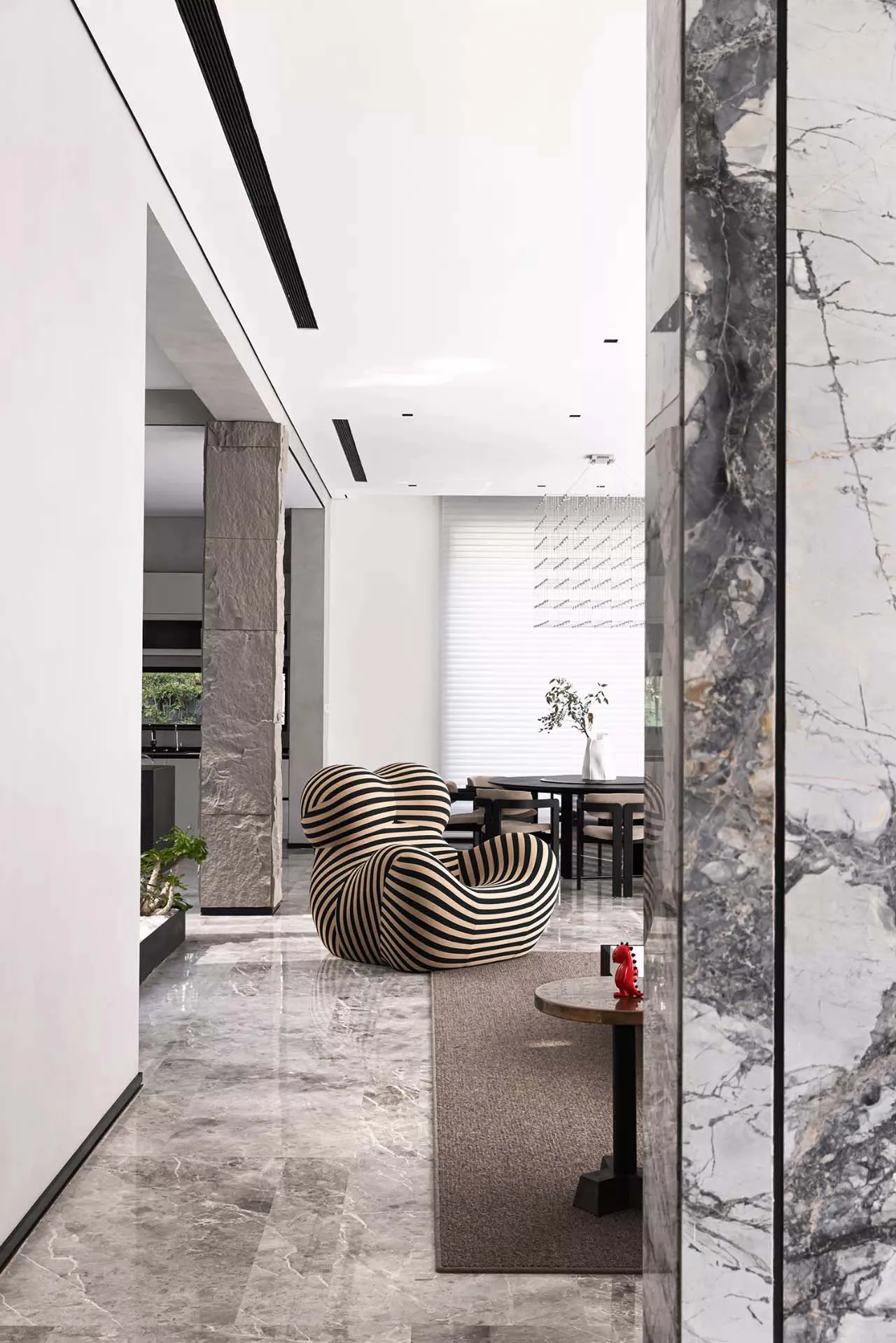 Modern, spacious living room with marble floor, a unique black and white striped lounge chair, and a small, elegant side tabl