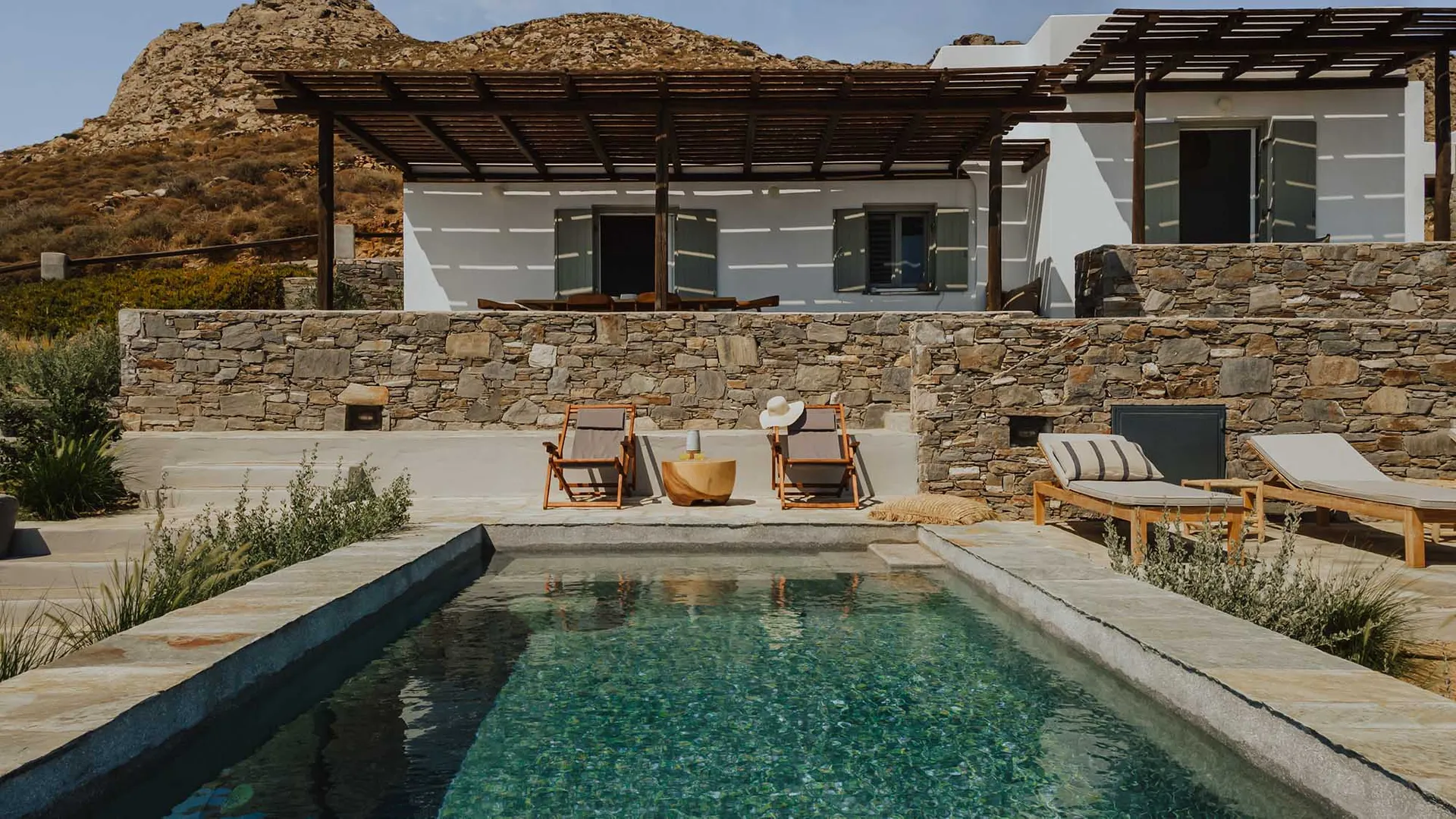 A minimalist vacation home with a concrete and stone exterior, featuring a pergola and a swimming pool.