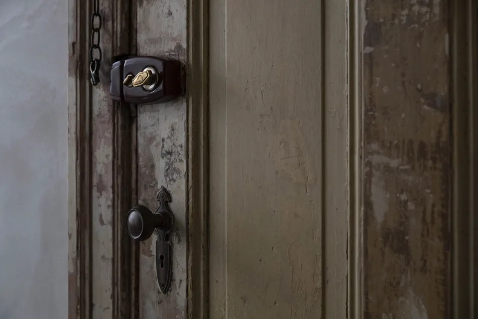Close-up of an aged wooden door with metallic lock and doorknob, showing signs of wear and paint chipping.