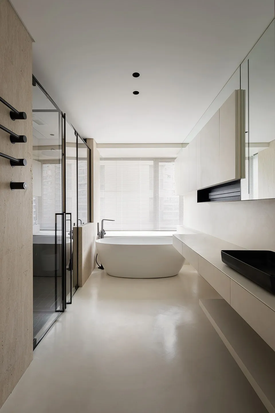 A minimalist modern bathroom with a large standalone bathtub in a concrete floor, white cabinets, and a glass shower enclosur
