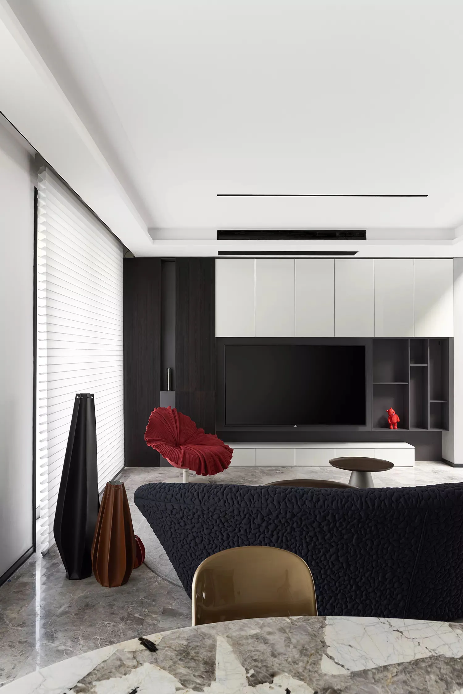 A modern living room featuring a textured black couch, a sleek black chair, and a marble floor. Modern design elements includ