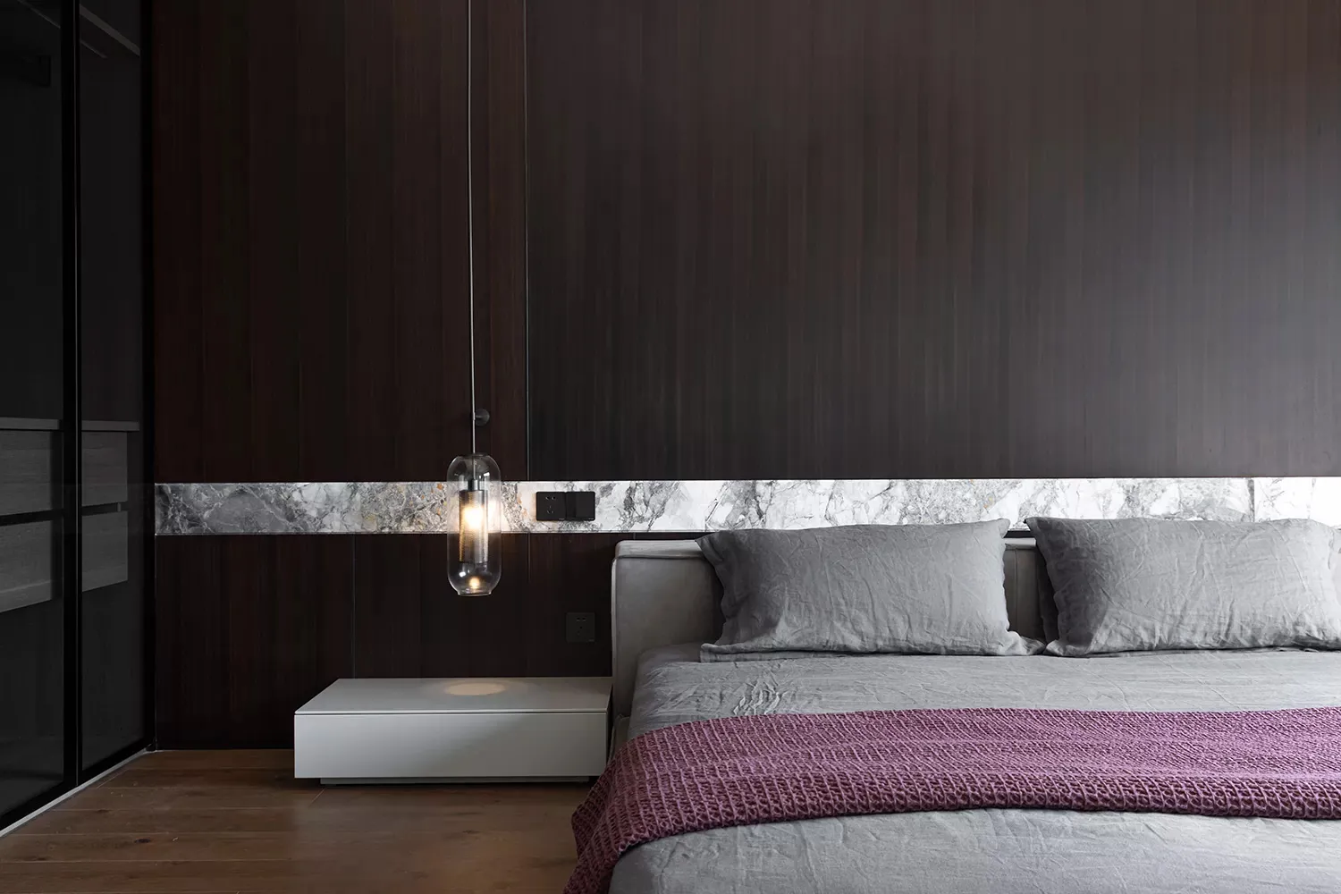 A minimalist bedroom with wooden walls, a grey bed, and a purple throw blanket.