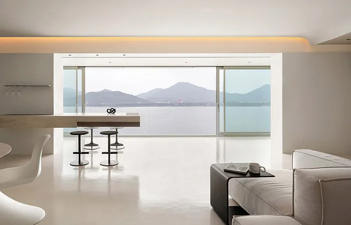Modern minimalist living room with concrete flooring, minimalist furniture, and large windows overlooking mountains.