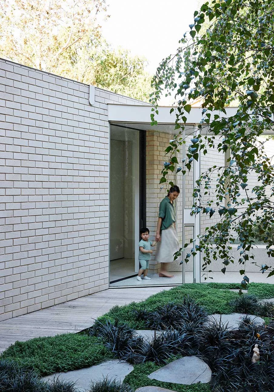A minimalist exterior residential building with brick, glass, and concrete materials, surrounded by lush greenery and yards.