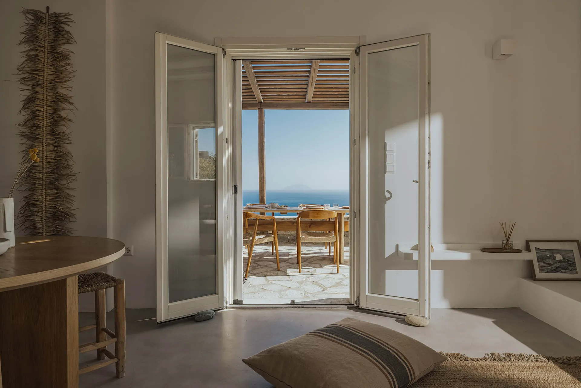 A minimalist home interior with an open door leading to a view of the sea, featuring wooden furniture and a serene atmosphere