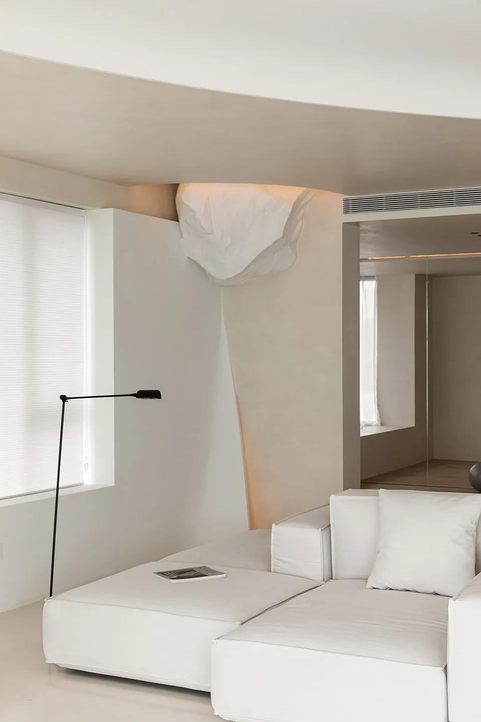 A modern minimalist living room featuring a white sofa, floor lamp, and geometric lighting fixture.
