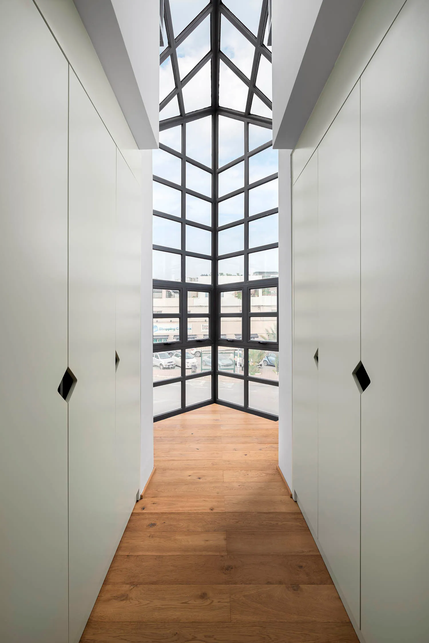 A modern, light-filled hallway with a glass ceiling and wooden floor.