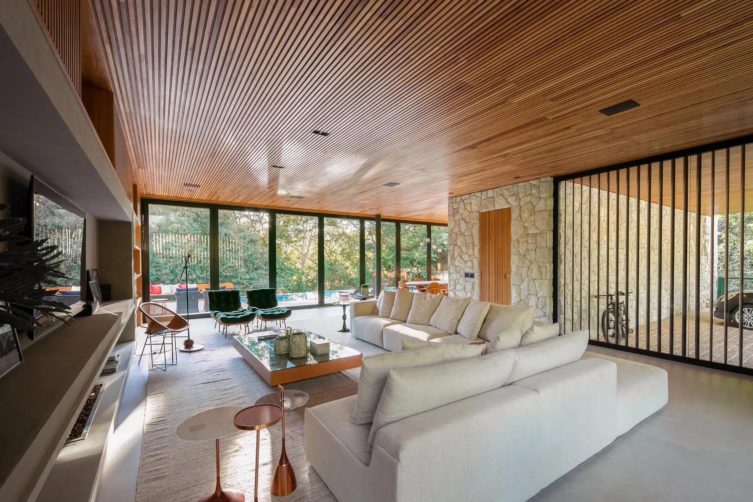 Modern living room featuring wood-paneled ceiling, glass walls, and stone fireplace