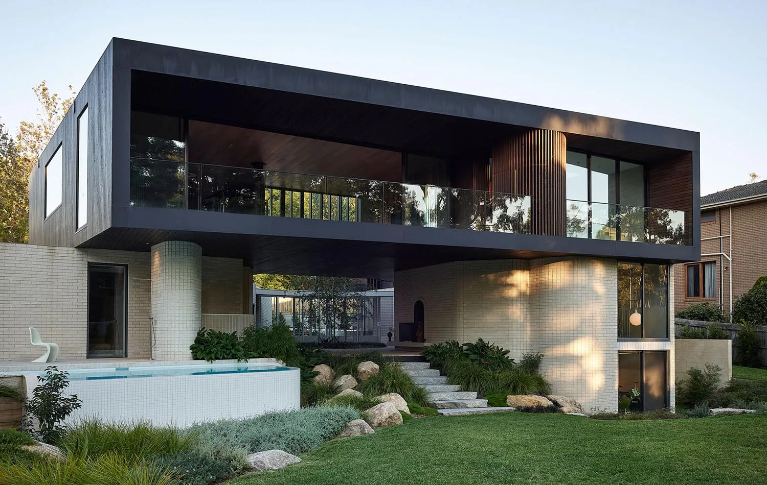 Modern residential exterior with brown brick cladding, concrete columns, and glass balustrades.