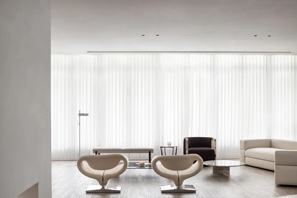 Modern living room with minimalist design, featuring white fabric furniture, glass table, and metal accents.