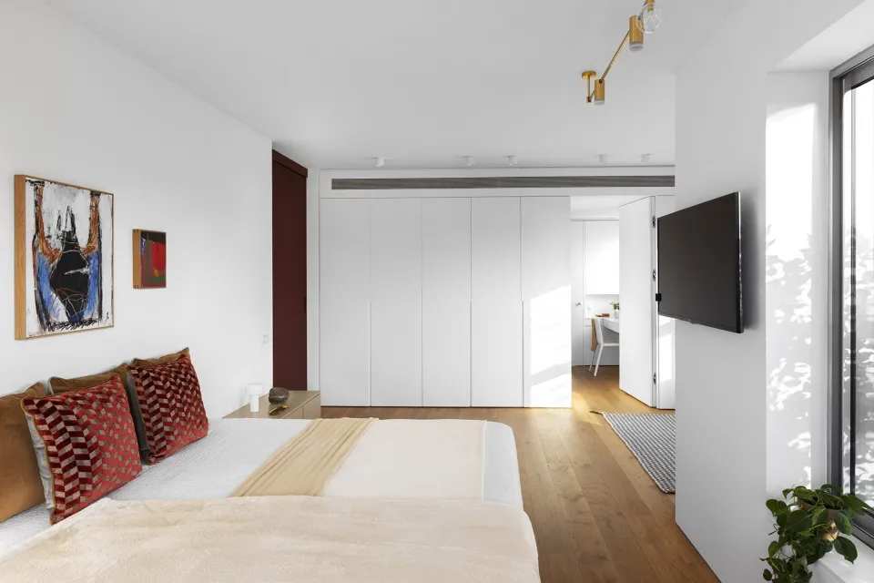 A modern, minimalist bedroom with a white bed, wooden floor, and minimalist decor.