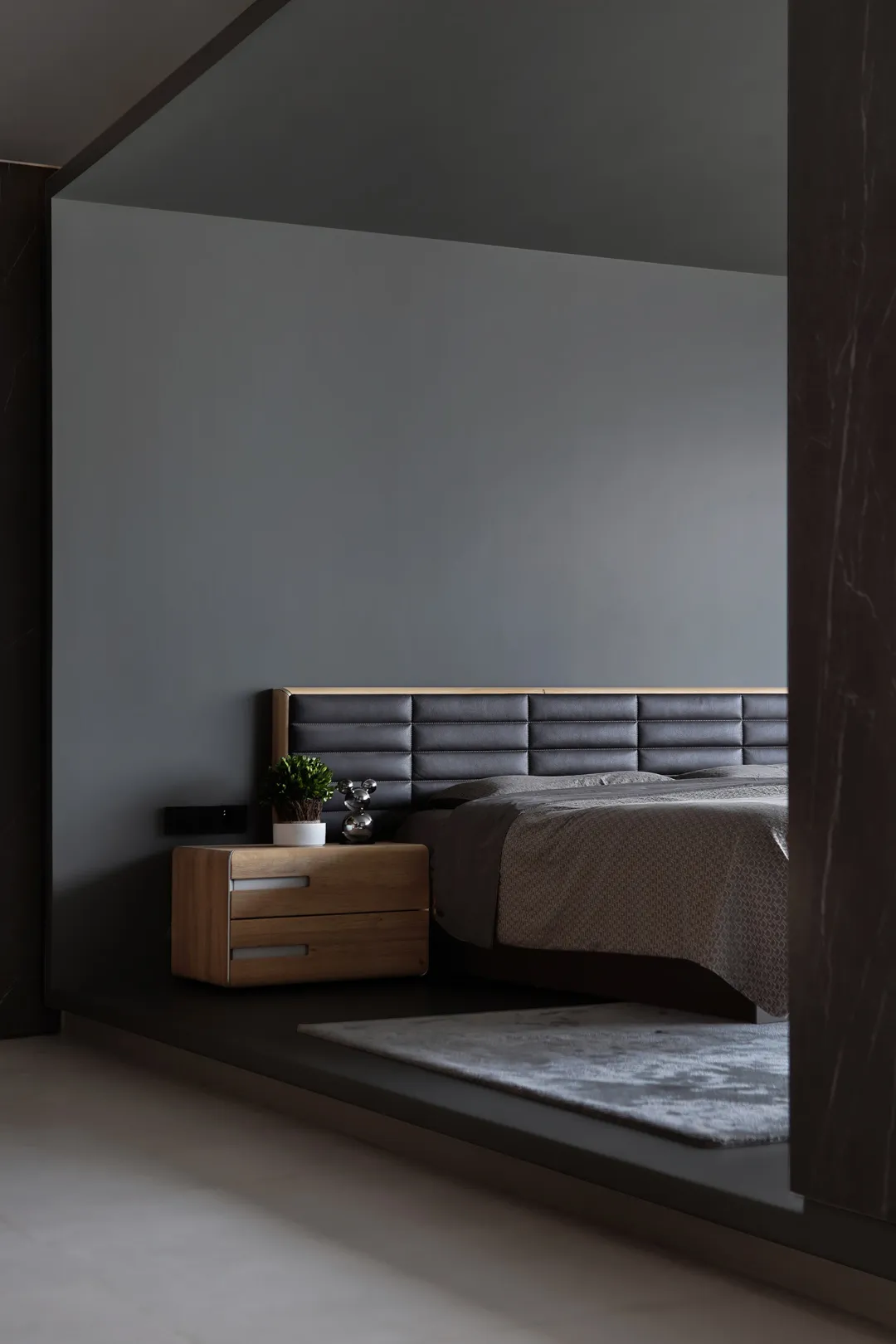 A minimalist bedroom featuring a wooden nightstand, a leather upholstered bed, and a textured blanket.