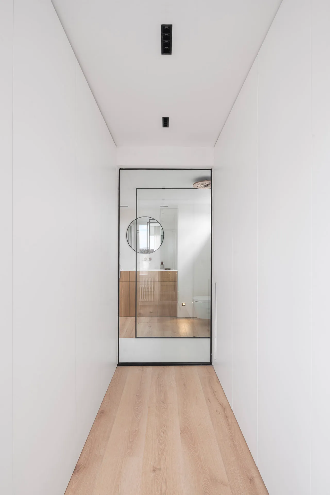 Modern bathroom with glass door and wooden floor.