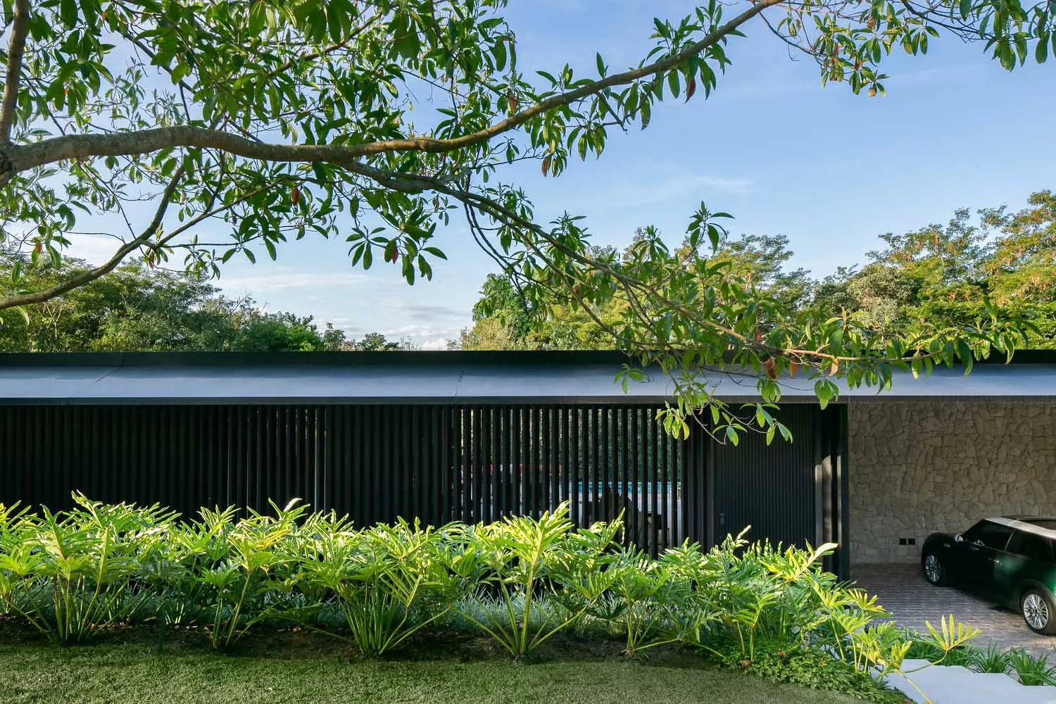 A modern house with metal panels and stone walls, surrounded by lush greenery.