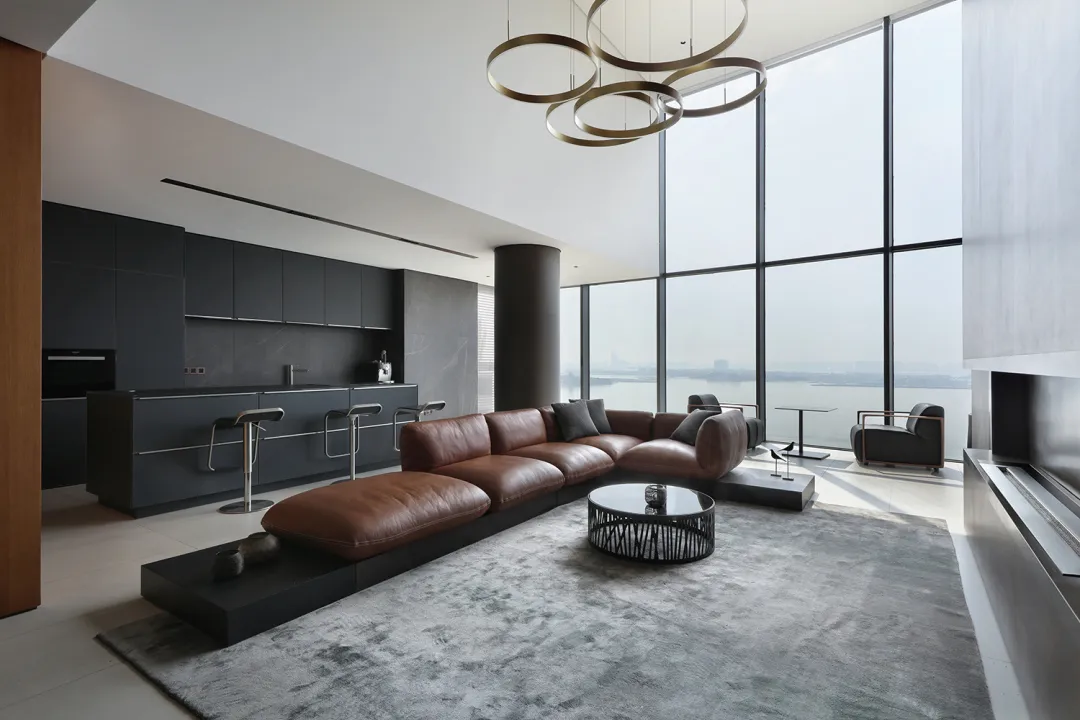 Modern living room with a leather sofa, coffee table, and large windows overlooking a body of water.