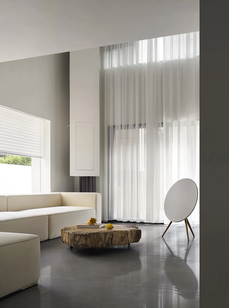 A modern, minimalist living room with white furniture, a wooden coffee table, and sheer curtains.