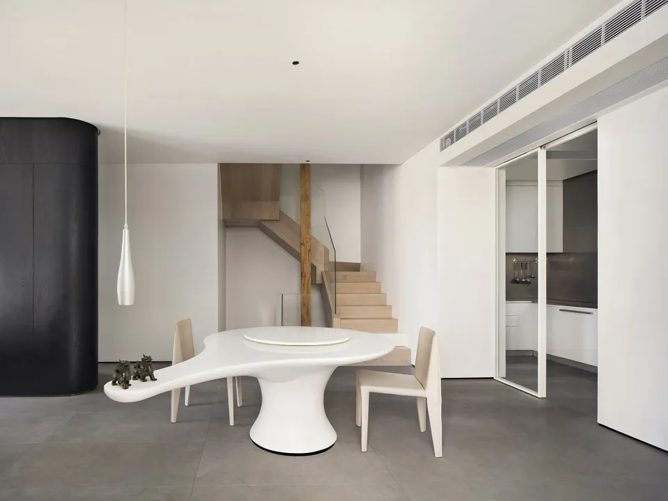 A modern, minimalist dining room featuring a sleek, white, organic-shaped table with a circular centerpiece, surrounded by th